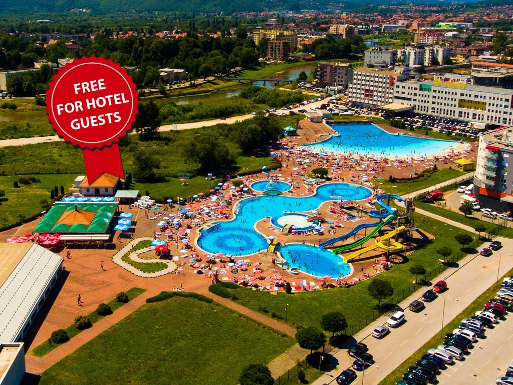 Hotel Hills Sarajevo Congress & Thermal Spa Resort Іліджа Екстер'єр фото The photo shows an aerial view of a large swimming pool area, likely part of a hotel or resort. There are several pools of different shapes and sizes, including one that resembles a Mickey Mouse shape. The area is filled with numerous sun loungers an